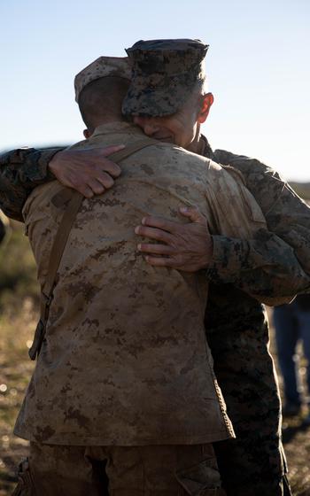 A Marine Corps colonel embraces his son, a Marine Corps private.