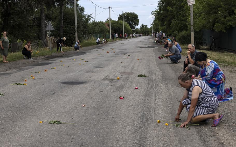 Mourners hold flowers and kneel await for the arrival of the coffin of Ukrainian soldier Oleksandr Babych in Krasnosillia, Ukraine, during his funeral on June 24, 2023.