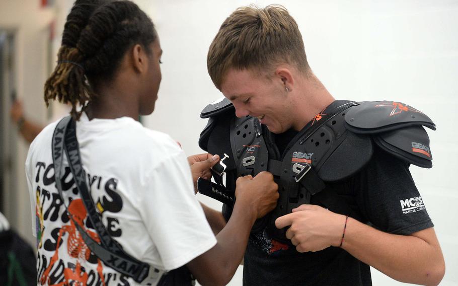 Junior Carlos Cadet helps fit fellow Kubasaki junior Jackson Nicolas' shoulder pads.