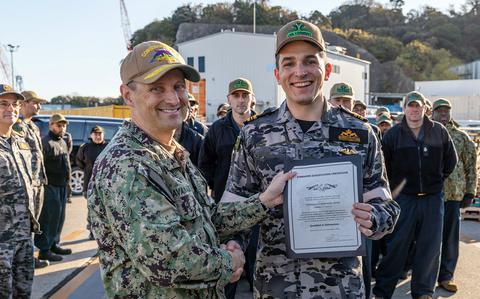 A man in an American military uniform shakes hands and holds up a certificate with a younger man in an Australian military uniform.