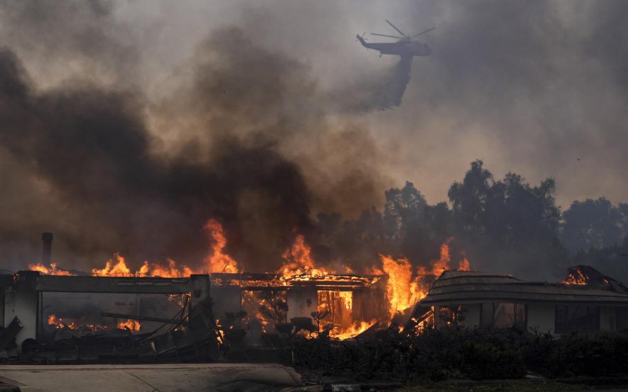 A helicopter pours water onto a burning house.