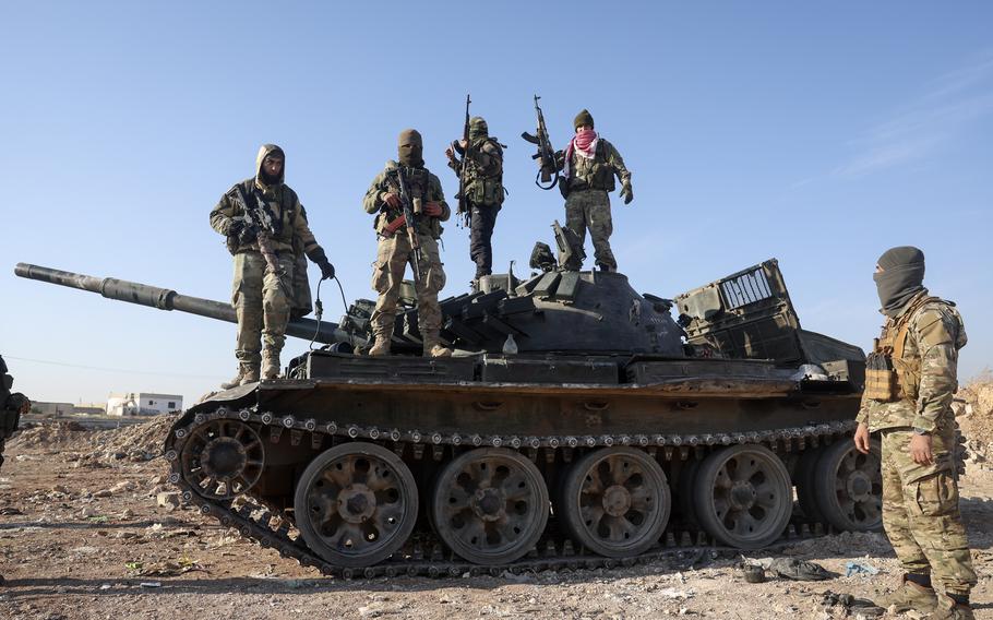 Syrian opposition fighters stand atop a seized Syrian army armoured vehicle