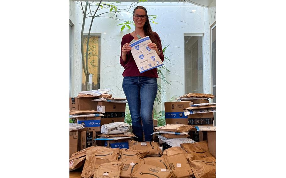 Caitlyn Webber stands, holding a packing envelope, with dozens of packages containing books at her feet.