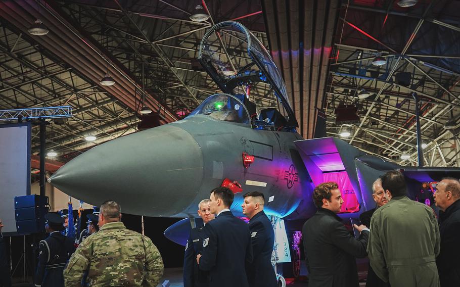 Service members and guests talk to each other in front of an  F-15 displayed in a hangar at RAF Lakenheath.