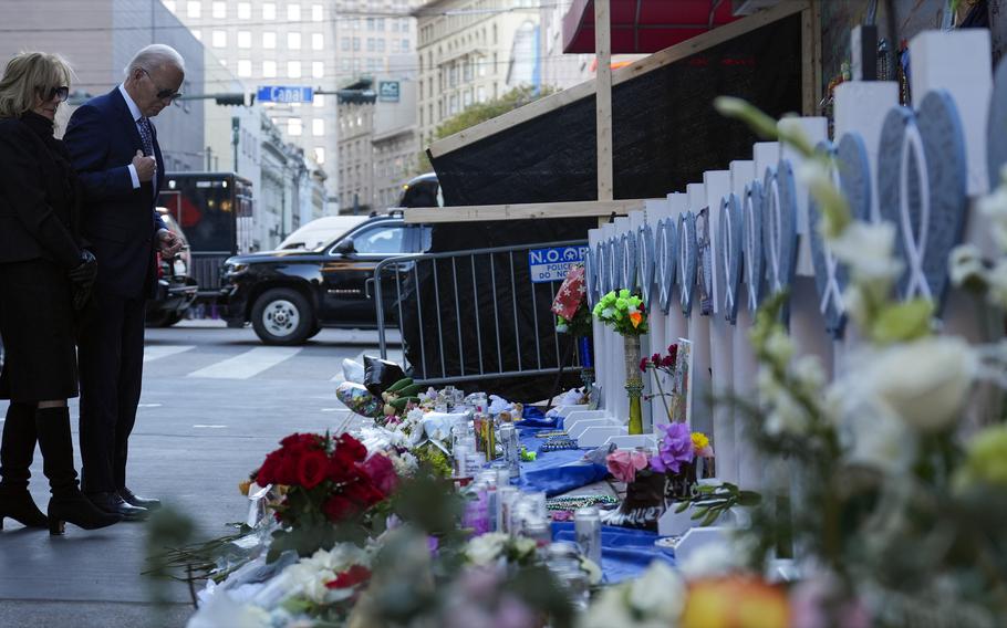 President Biden and first lady Jill Biden standing on the left side of the image and looking down at a makeshift memorial placed on the ground. 