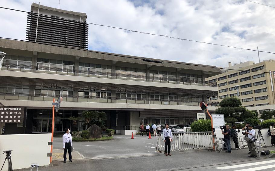 Reporters holding camera equipment are shown outside a building. 