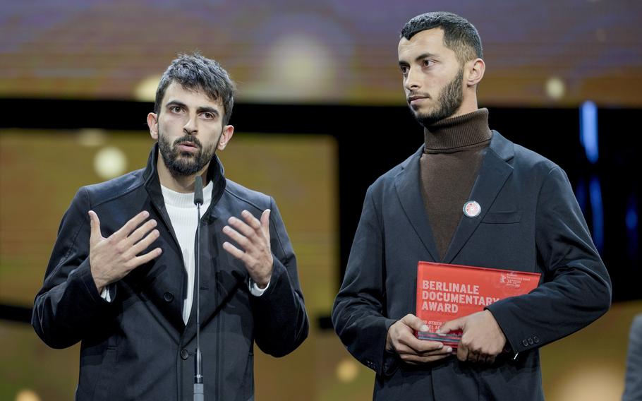 The two primary creators of the documentary “No Other Land” speak into a microphone while receiving an award for the film.