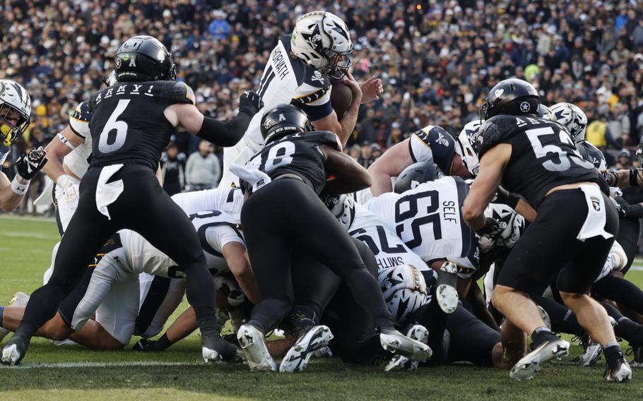 The Navy quarterback leaps over the line of scrimmage and Army defenders to score a touchdown.