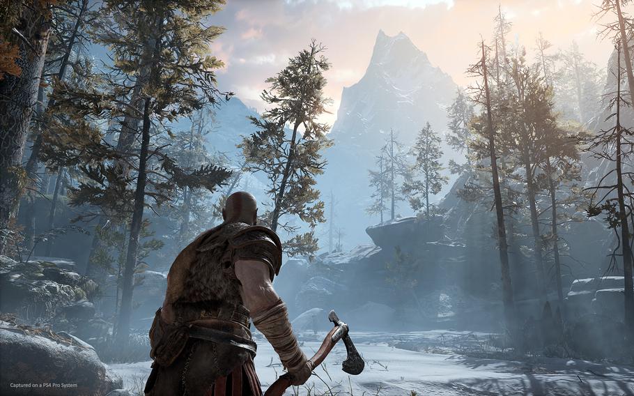 A man holding a hatchet-like weapon looks out over a rocky, forested landscape in a frame from the video game God of War.