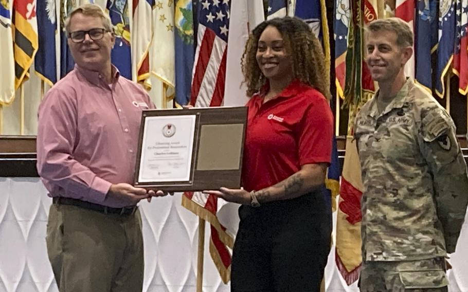 A Red Cross employee receives an award while flanked by military personnel.