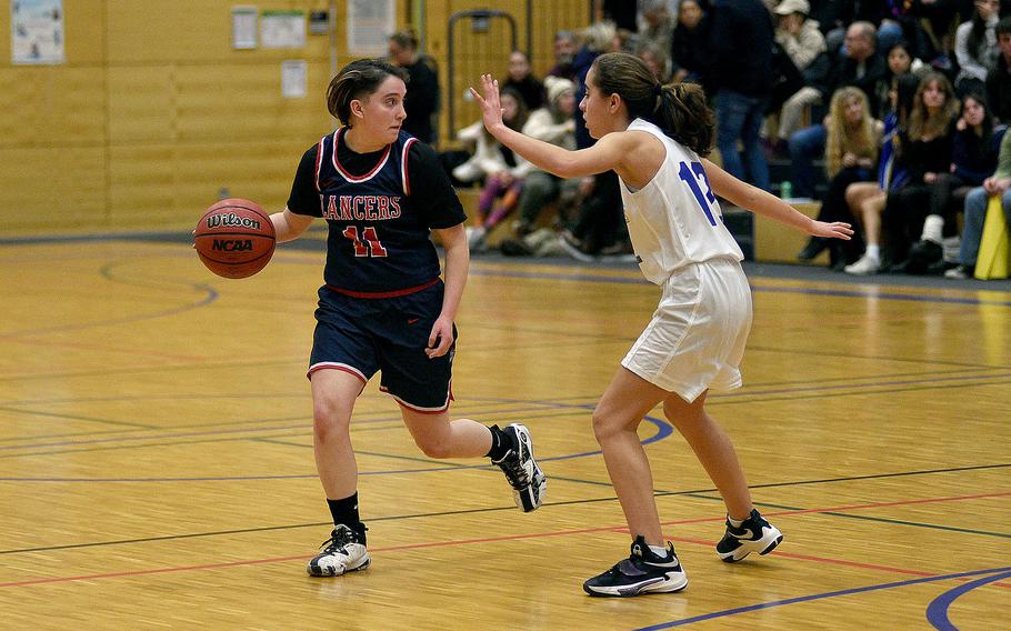 Lakenheath's Hailey Buchanan surveys the floor as she dribbles during a Dec. 1, 2023, game at Wiesbaden High School in Wiesbaden, Germany. Warrior Angelica Shea defends on the play.