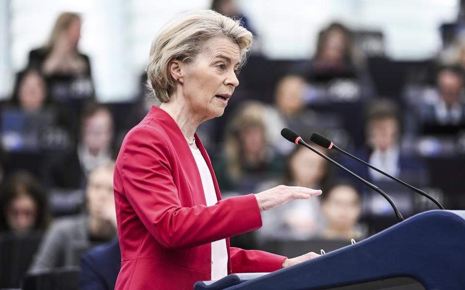 The European Commission president speaks at a podium in a red suit, seen from the side.