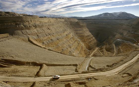 A white pickup truck drives down a road into a deep, barren mine.