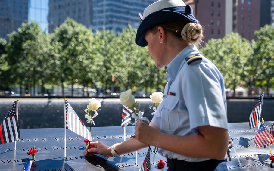 A woman in a Coast Guard uniform places flowers into a memorial plaque.