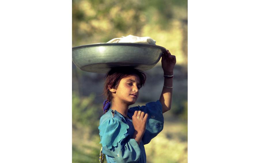 A young girl carrying a pan of cheese on top of her head