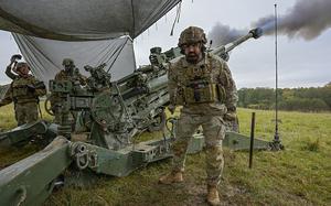 A soldier stands in front of a M777 howitzer with smoke coming from it. 