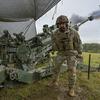 A soldier stands in front of a M777 howitzer with smoke coming from it. 