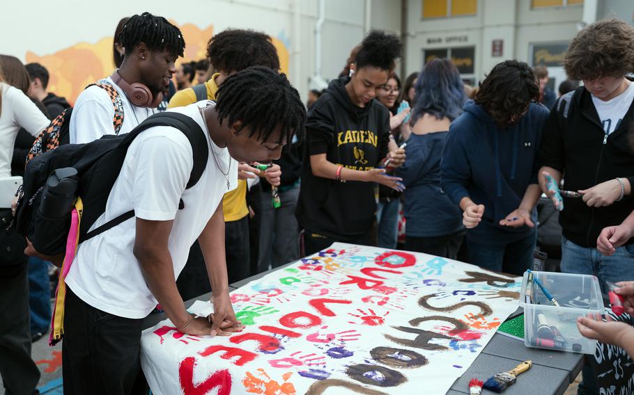 Kadena High School students cover their hands in paint to leave handprints on a banner that reads, “ Our Voices, Our Schools.”