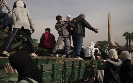 A Syrian child points a rifle towards the sky while on top of a government tank.