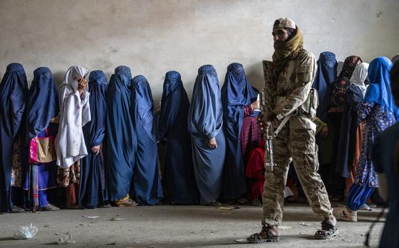 A Taliban fighter stands guard as women wait to receive food rations ...