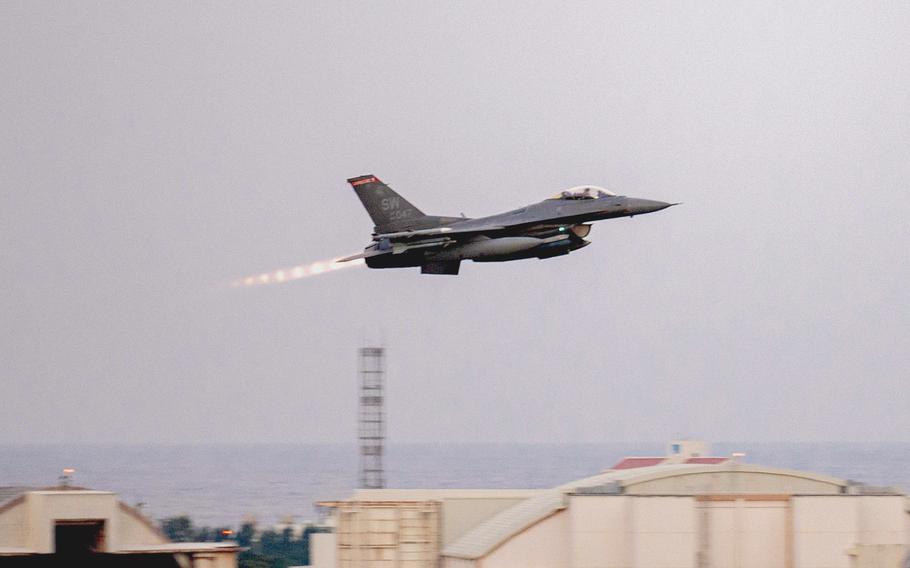 A fighter jet rises above buildings on a military installation as it takes off.