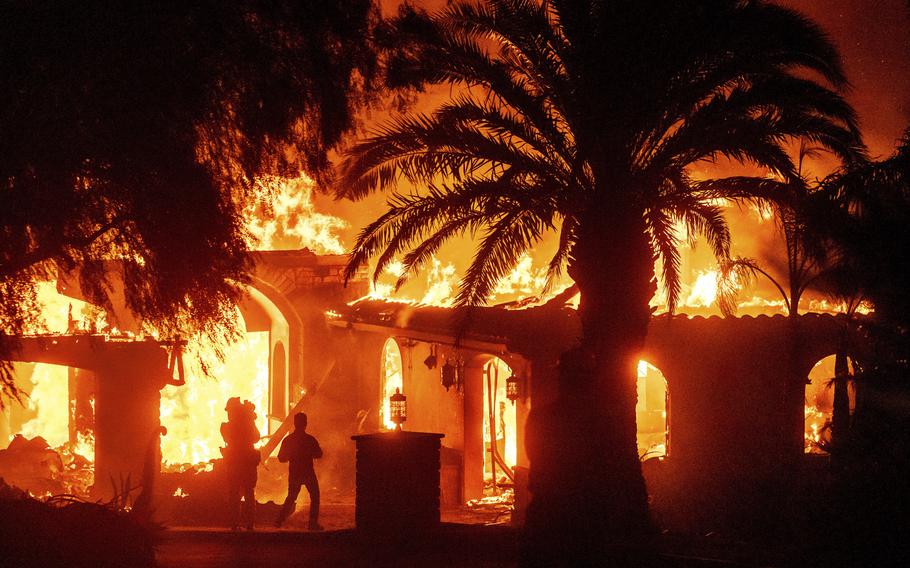 Television reporters film as flames from the Mountain Fire consume a home