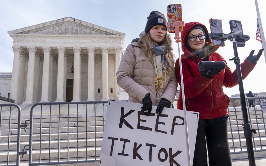 Two people standing in front of gates in front of the Supreme Court building, facing phones on stands.