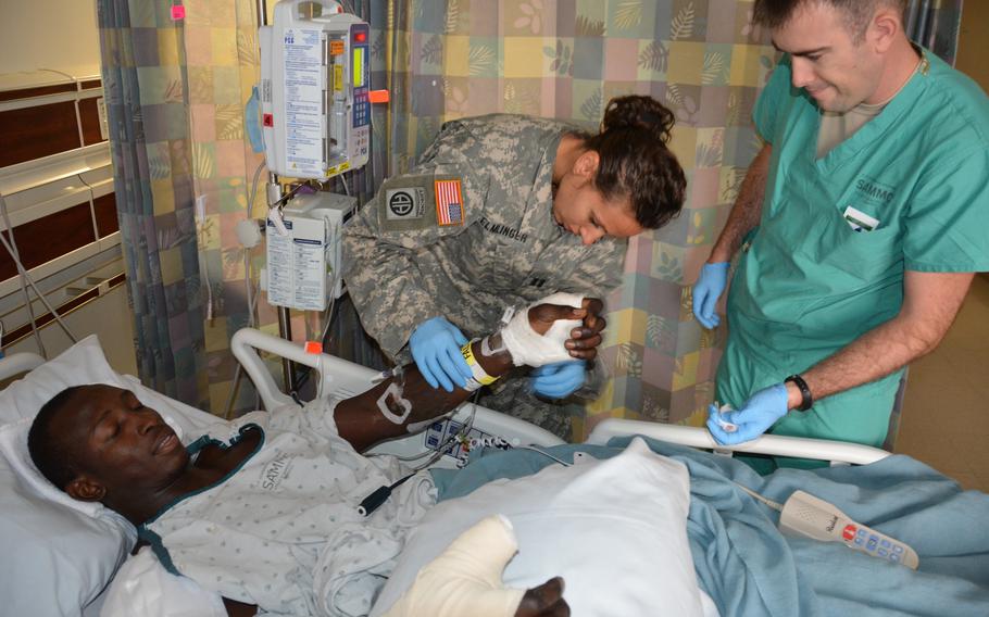 Then-Capt. Kelly Elmlinger, an Army nurse, checks on patient Papa Ndiaye while Army Spc. Jeremy Allred looks on in the 4 West inpatient ward at San Antonio Military Medical Center, Oct. 23, 2015. 