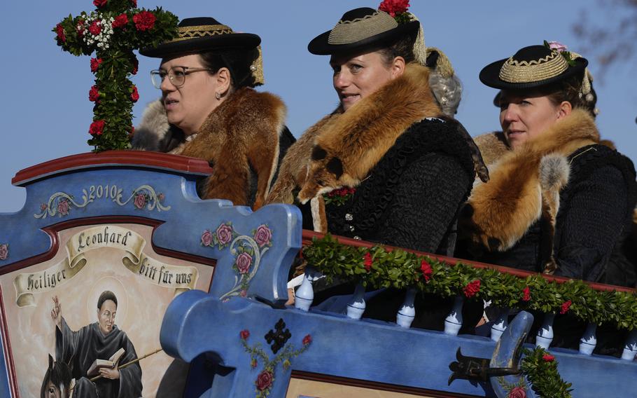 Women wearing traditional costumes ride in a carriage during a pilgrimage.