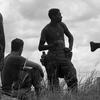 A Marine holds a canteen while standing next to a seated Marine in a grassy field.