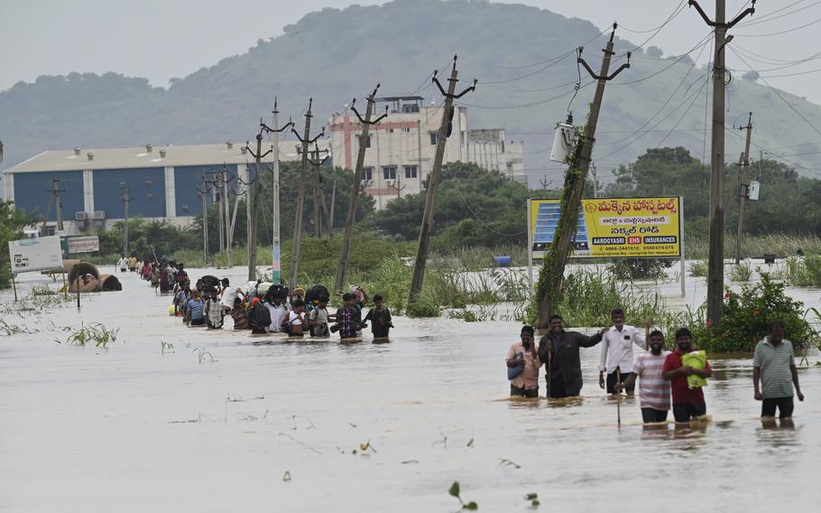 People, many carrying their belongings, wade through a flooded road