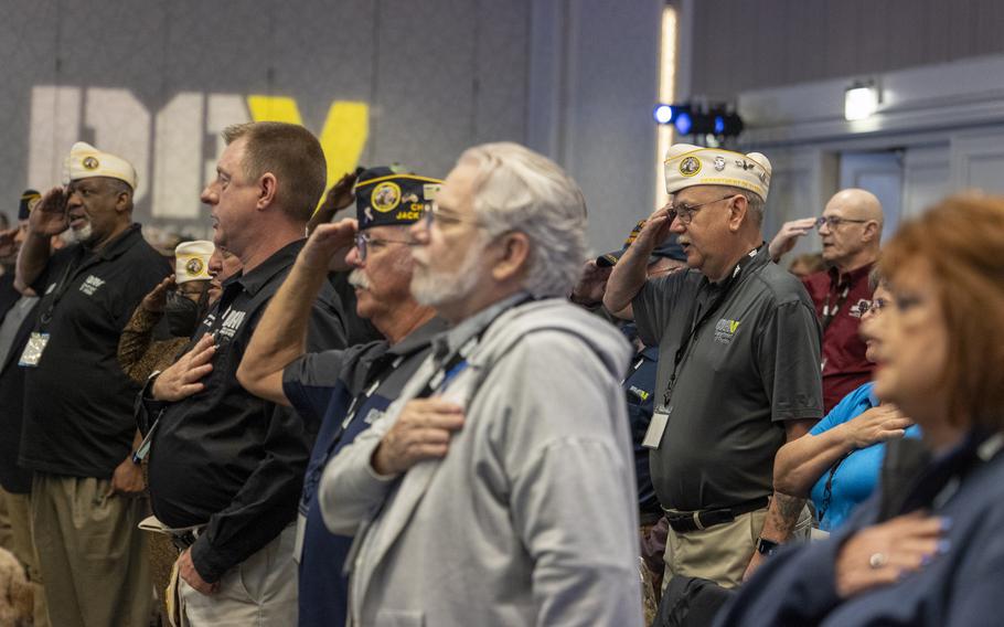 A crowd of veterans, some saluting and others with their right hand on their chest.