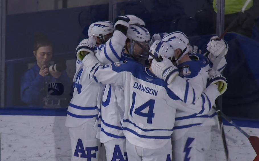 Hockey players in white and blue huddle with their hands on each other’s helmets and shoulders.