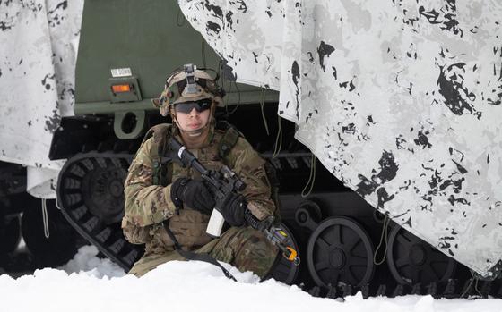 A soldier with the Alaska-based 11th Airborne Division crouches near a military vehicle.