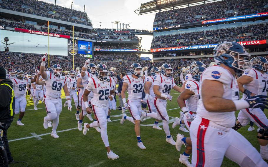 Navy football players run on the field wearing uniforms inspired by NASA, with the logo on the shoulder.