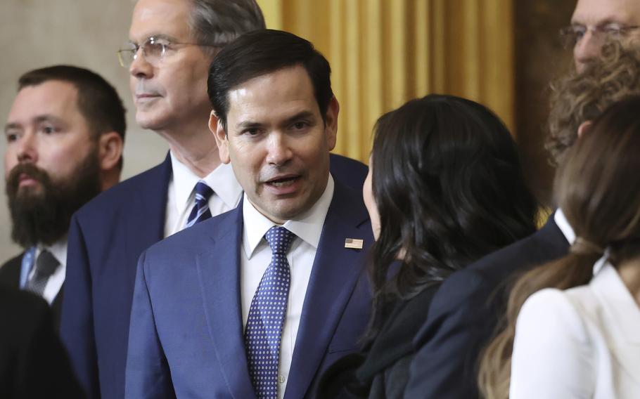 Marco Rubio wearing a blue suit and tie speaks to a woman.