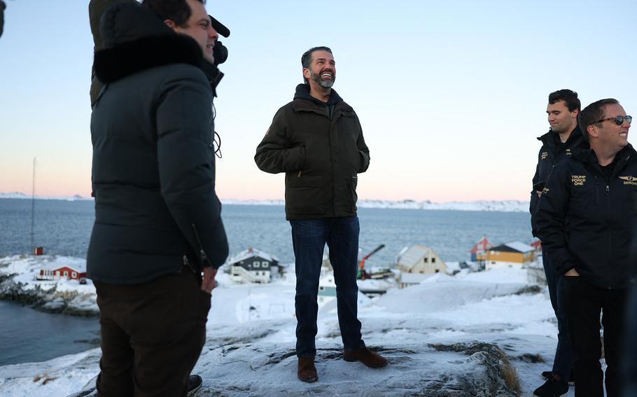 A few men stand on an icy hill overlooking a few small buildings by the sea.