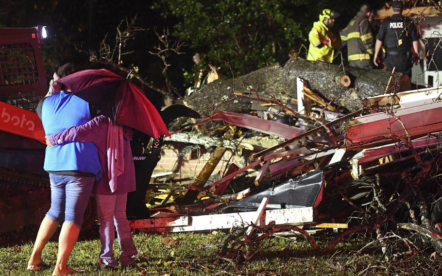 Bystanders embrace in front of wreckage after a tornado.