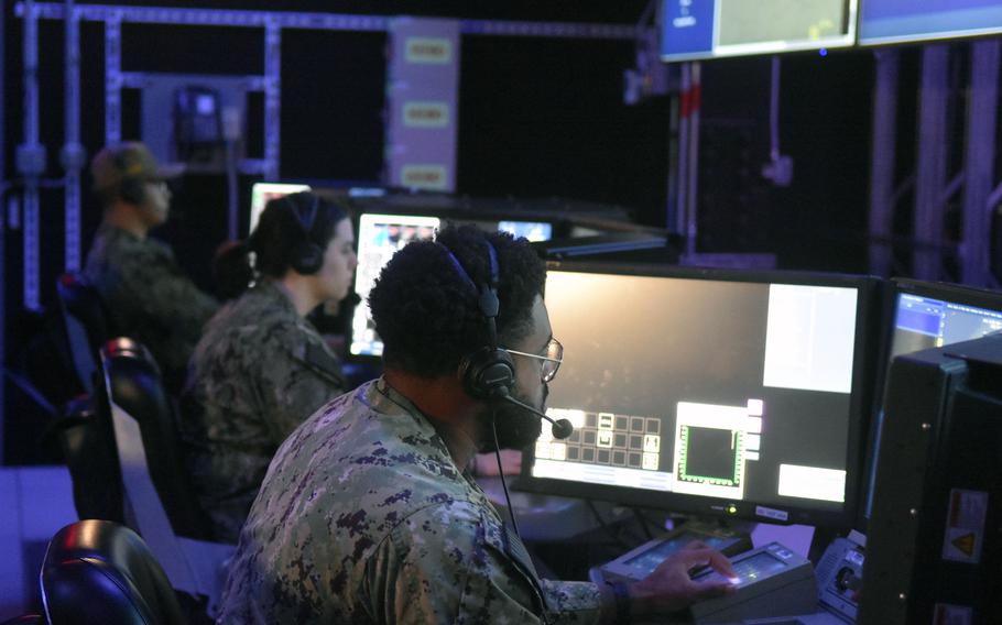 Sailors sit at computer screens wearing headphones.