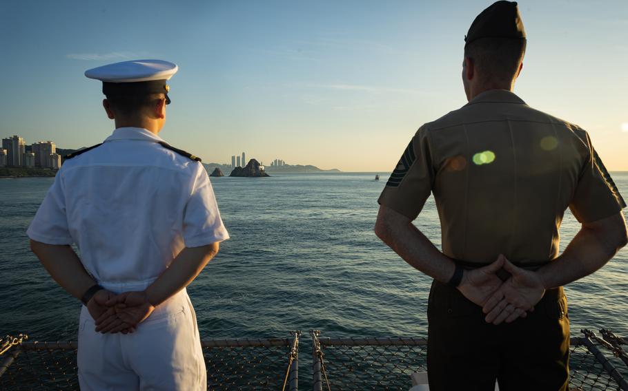 A sailor attached to the amphibious assault ship the USS America, left, and a Marine attached to the 31st Marine Expeditionary Unit man the rails during a scheduled port call to Busan, South Korea, on Sept. 5, 2024.