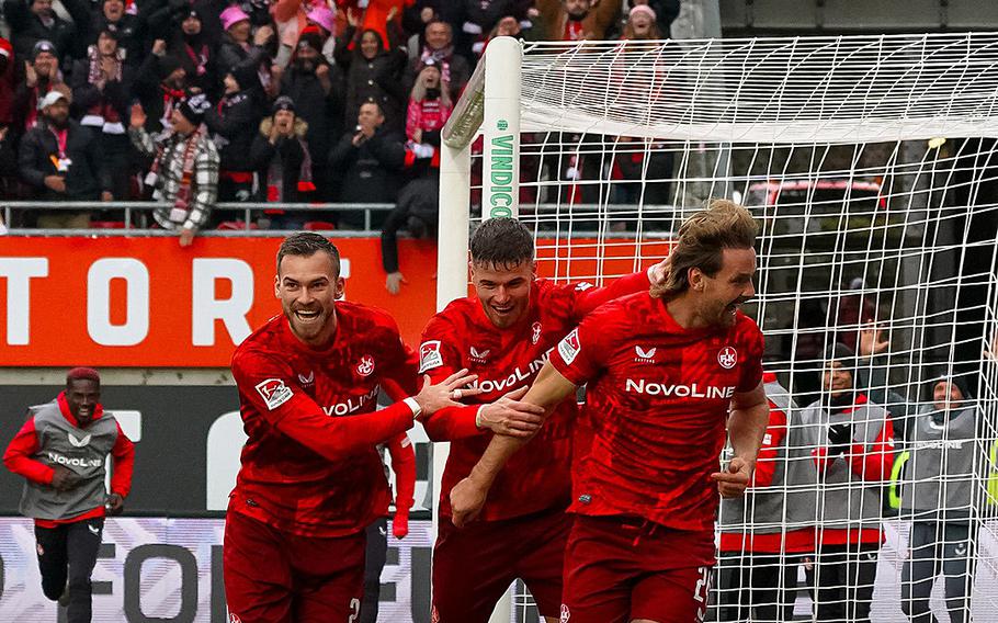 Three Kaiserslautern players in red grin as they celebrate a goal.