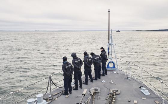 Sailors stand aboard part of an Estonian naval ship and look out at the sea.