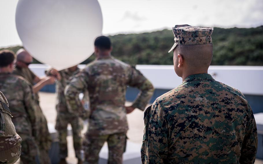 A U.S. Marine observes U.S. Army soldiers preparing to raise a tethered high-altitude balloon.