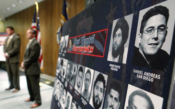 FBI officials in suits stand next to a large poster showing photos of wanted terorism suspects.