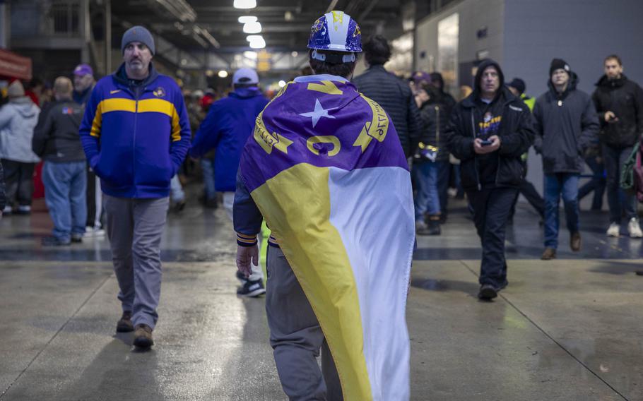 A man wearing a purple safety hat and a cape walks through a stadium.