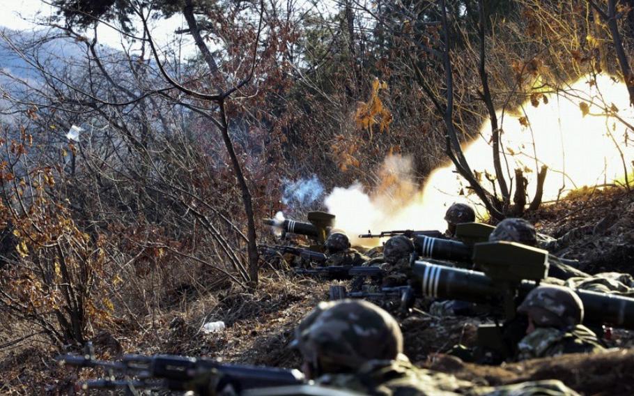 North Korean troops fire a weapon in a wooded area.