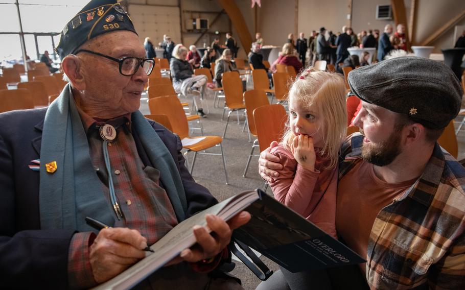 WWII veteran Ceo Bauer, on the left, signs a book for Air Force Maj. Christian Maude and his young daughter.