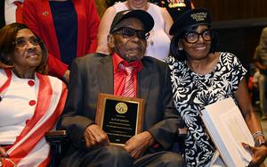 A man sits between two women while holding a plaque.