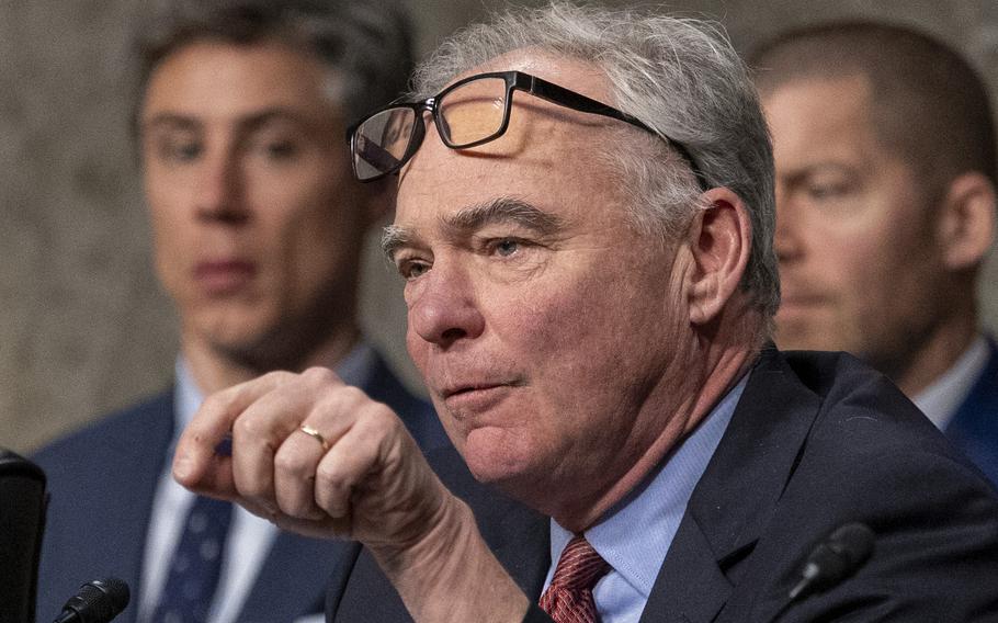 Kaine with his eyeglasses resting on his forehead gestures with his left hand as he speaks.