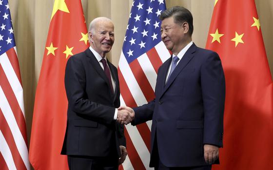 President Joe Biden shakes hands with Chinese President Xi Jinping while standing in front of a row of United States and Chinese flags.